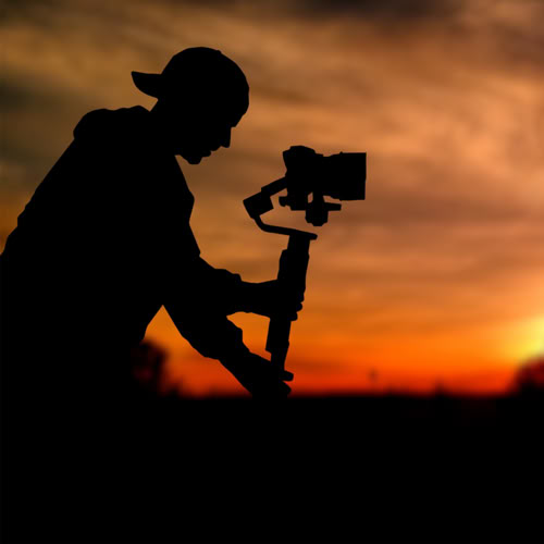Videographer silhouette with a camera on a gimbal against a sunset sky.
