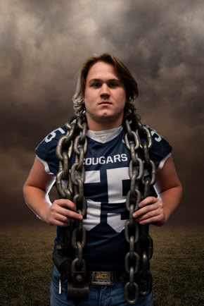 A person wearing a football jersey with the number 55 and the word "Cougars" holds large chains around their shoulders, standing against a cloudy sky background.
